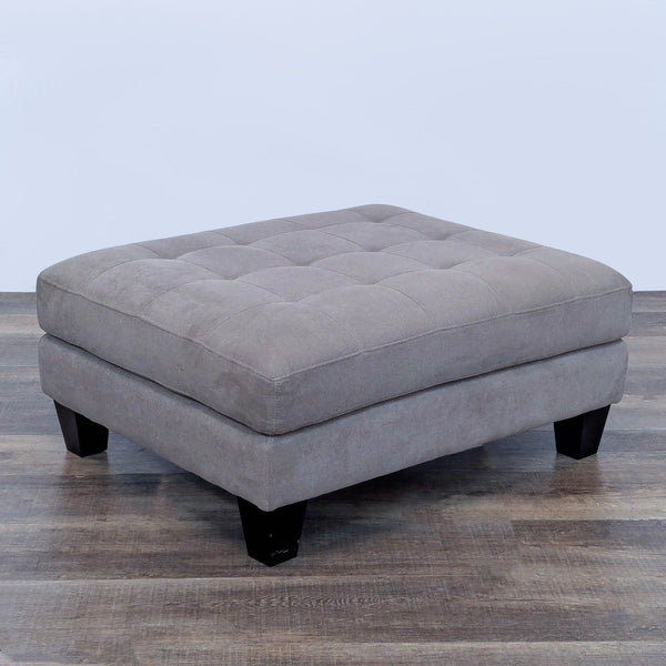 Gray rectangular ottoman with tufted top and dark wooden legs.