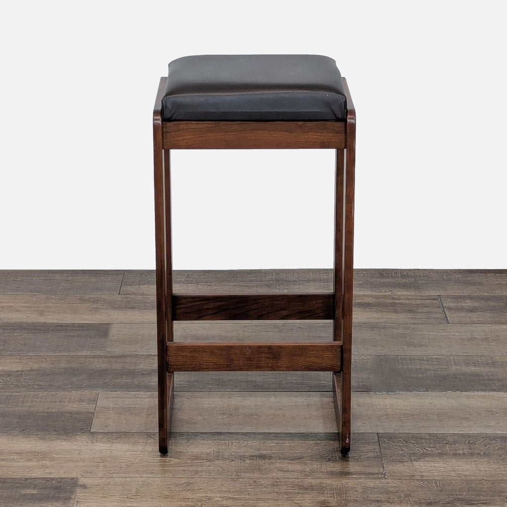 Wooden stool with dark cushion on wooden floor.