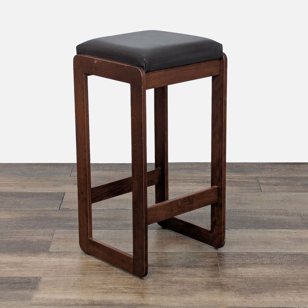 Angled view of a wooden stool with cushioned top.