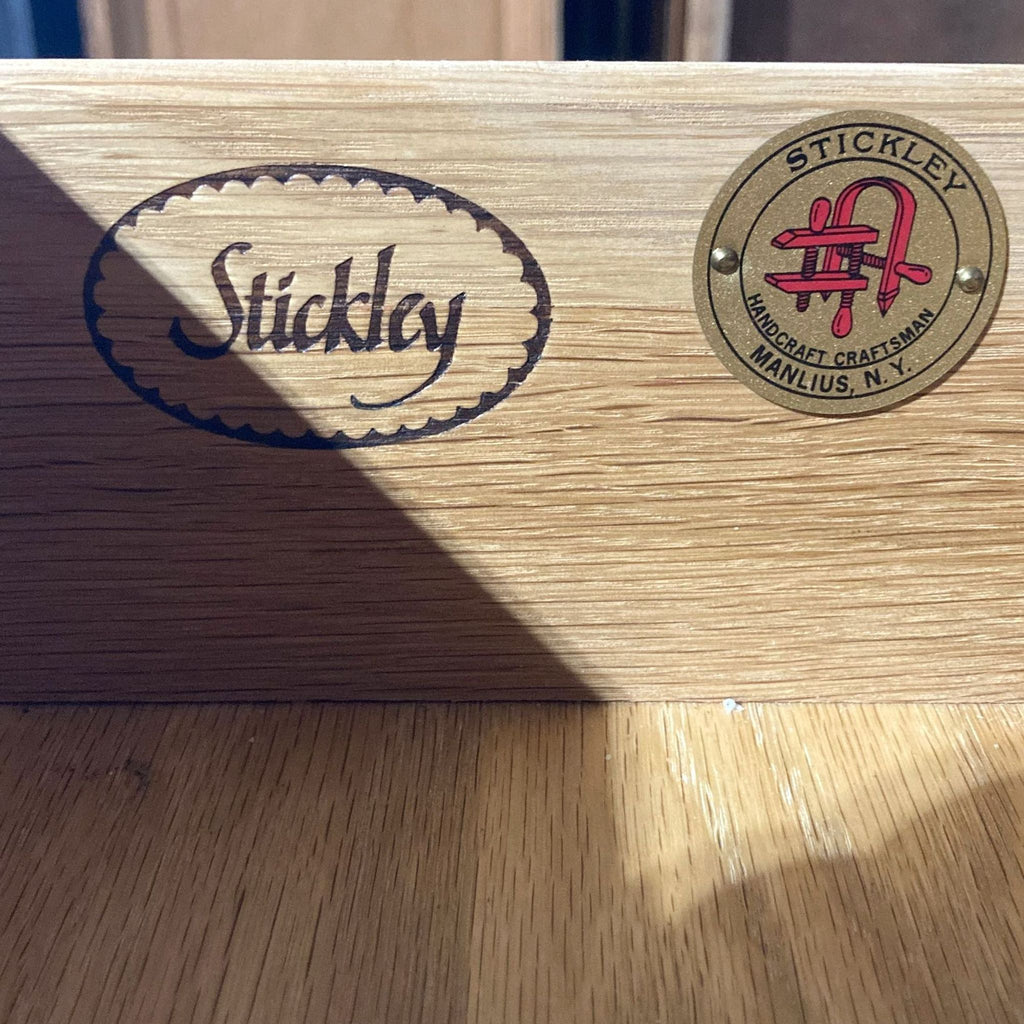 Stickley brand emblem and craftsmanship badge on wood surface.