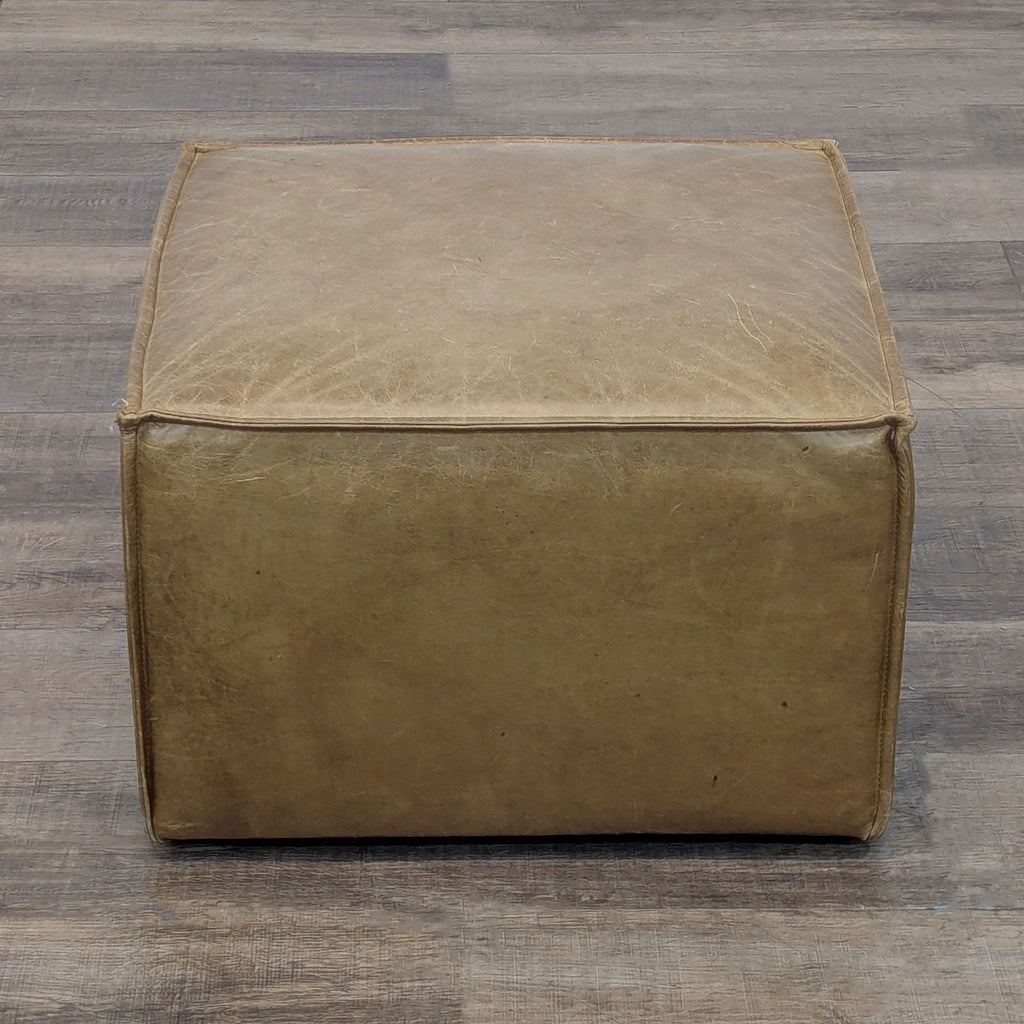 West Elm tan leather ottoman, cube-shaped on a wooden surface.
