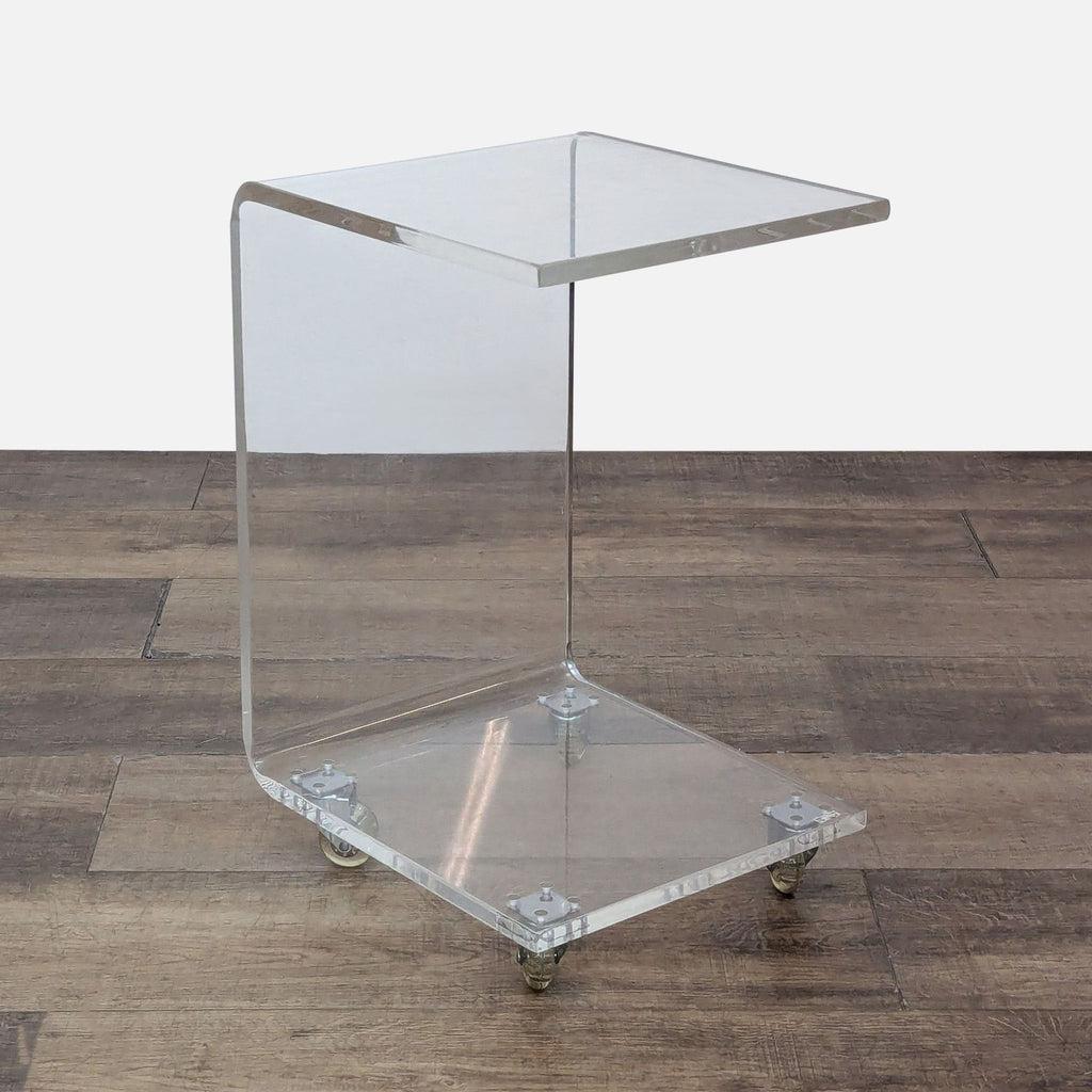 Clear acrylic side table with caster wheels on wood floor.