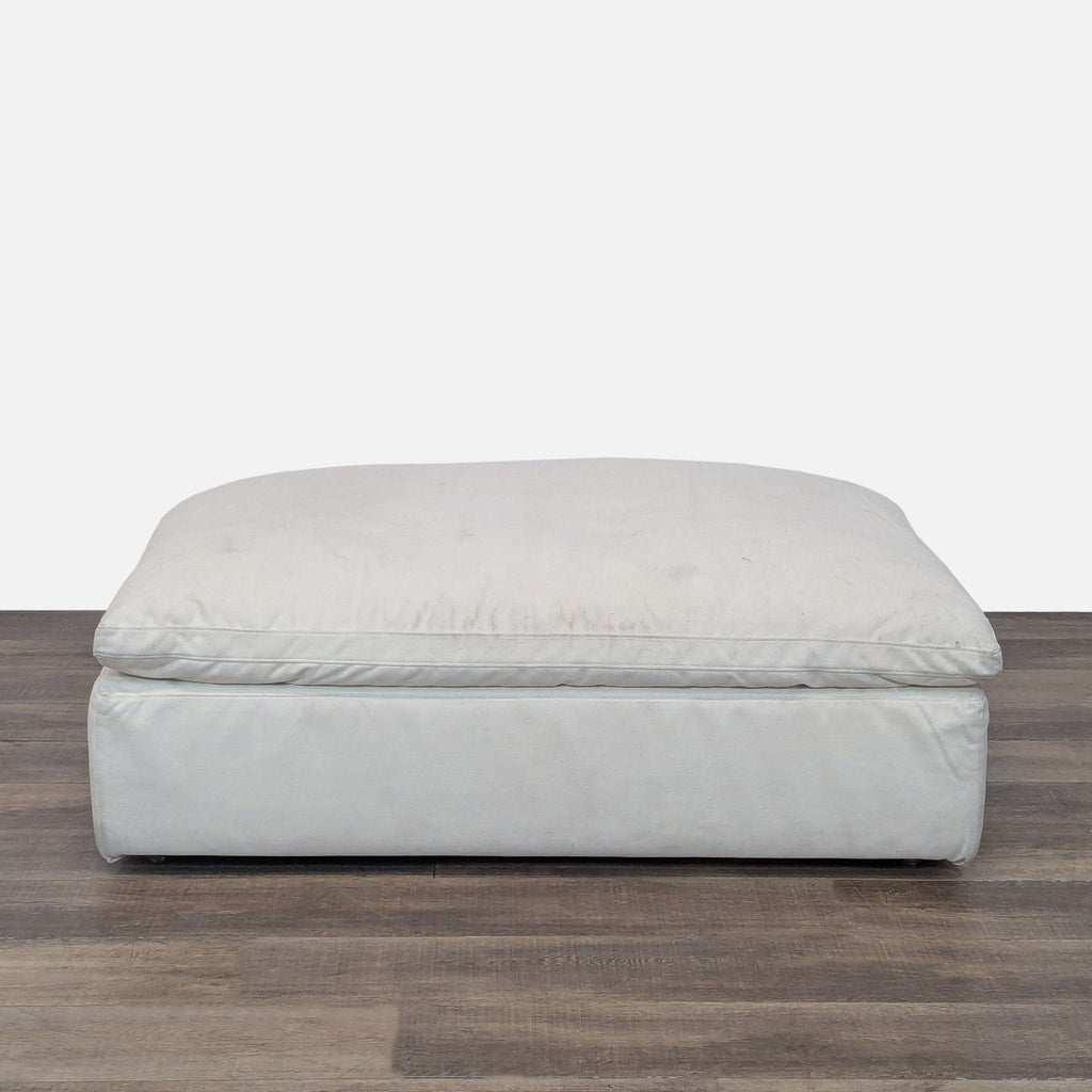 Side view of a spacious, cushioned RH ottoman on wooden flooring.