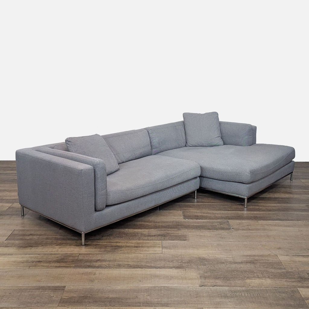 Angled view of gray sectional with chrome base and pillows.