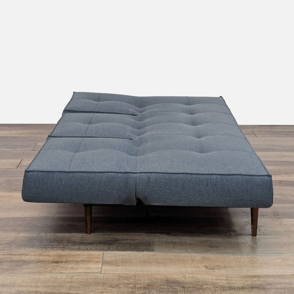 Sleeper sofa fully reclined to form a flat surface, with tufted detail.