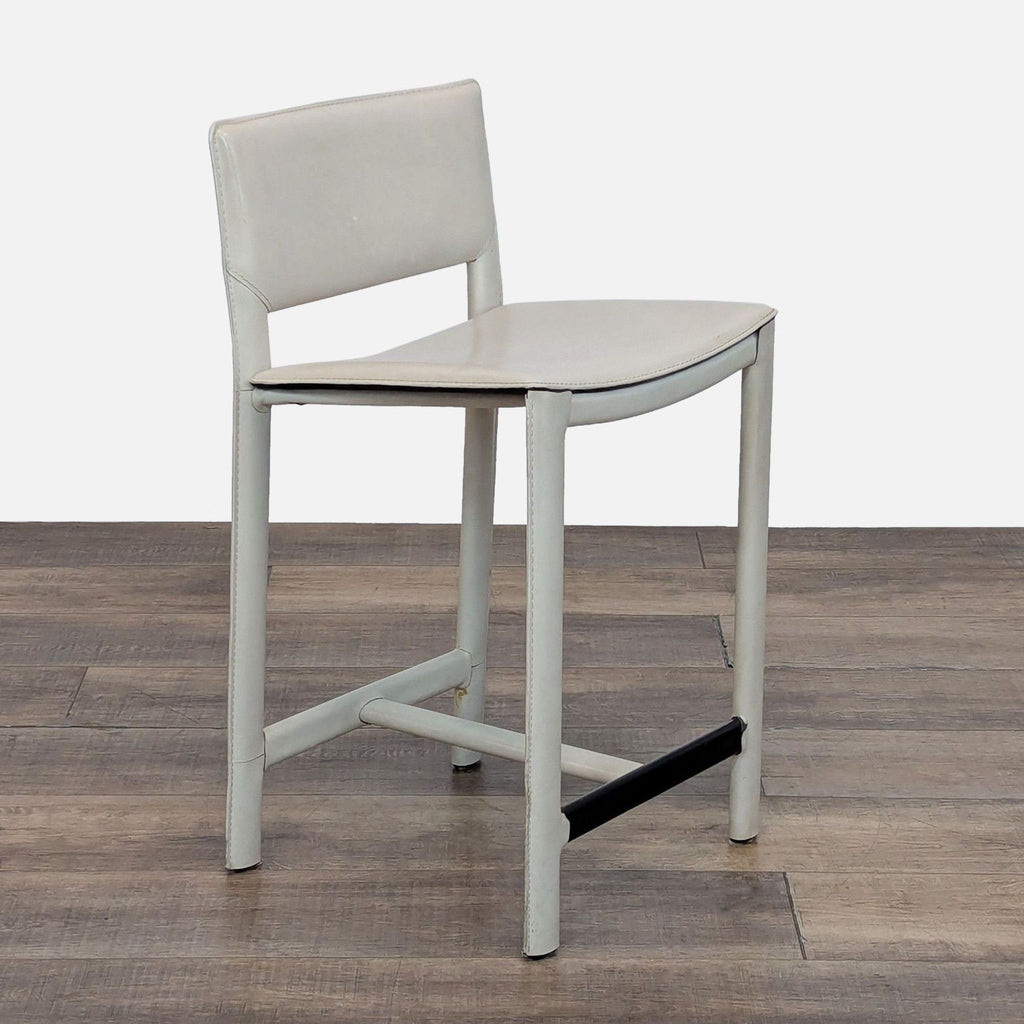 Side angle of a sleek, cushioned stool with a metal footrest.