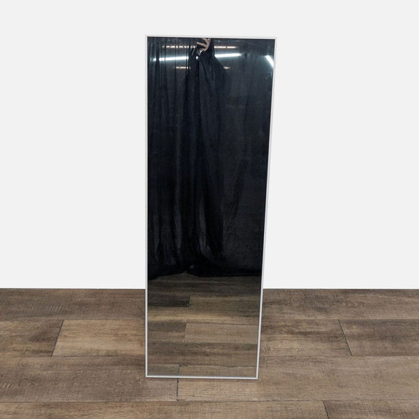 Tall rectangular mirror with white frame on wooden floor.