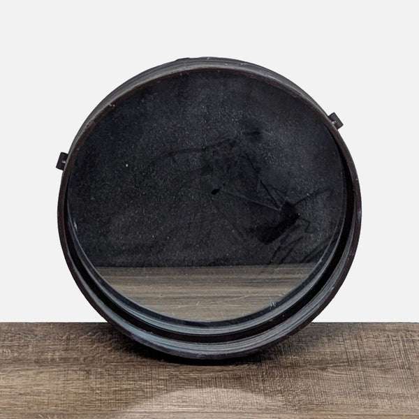 Round black mirror with a reflective surface on a wooden table.