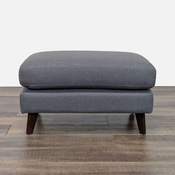 Gray ottoman with wooden legs on a wood floor, brand Living Spaces.