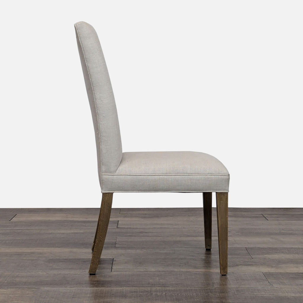 Side profile of a dining chair with wooden legs and light linen fabric.  