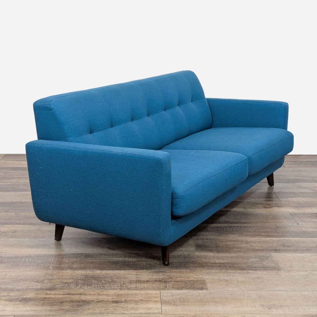 Angled view of a tufted blue loveseat on wooden floor.