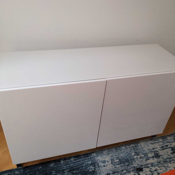 1. White Ikea cabinet with two doors, shown closed and placed against a wall on a wooden floor.