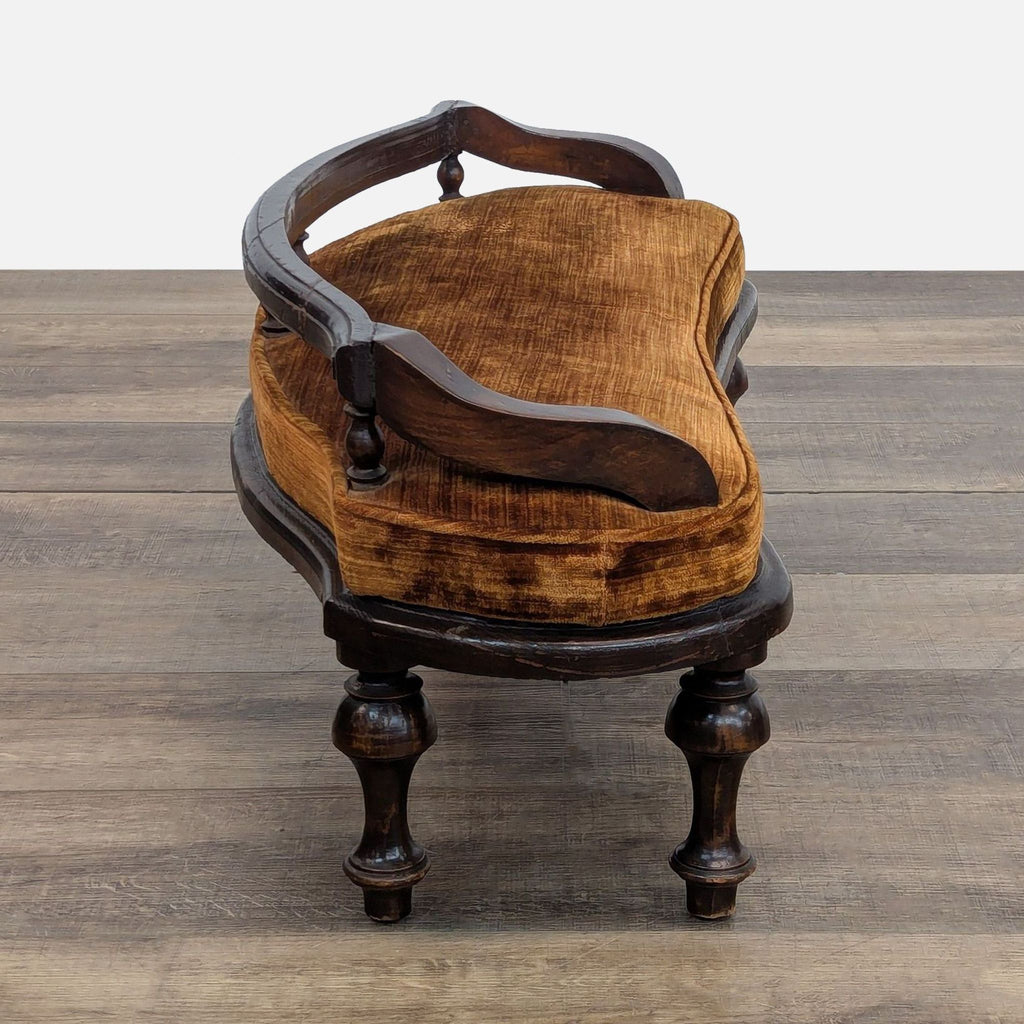 Curved antique bench with a plush brown cushion and detailed woodwork, set on a wooden floor.