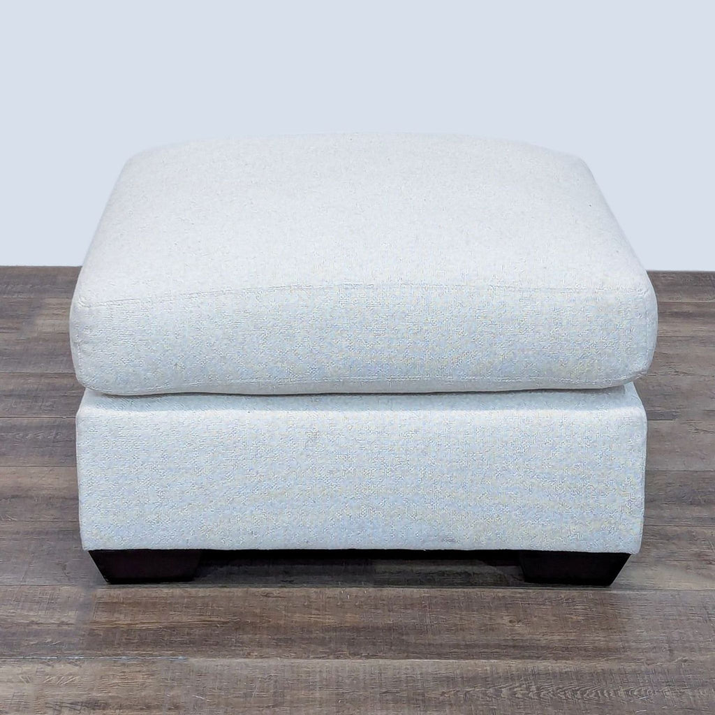 Light gray cushioned ottoman from Pottery Barn, featuring dark wooden legs.