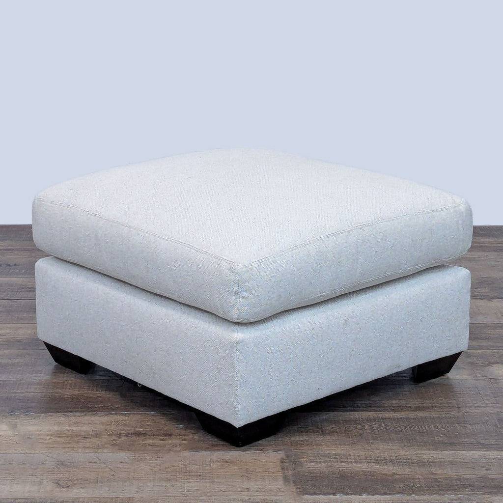 Square ottoman with a down blend cushion and rubberwood feet, on a wooden floor.