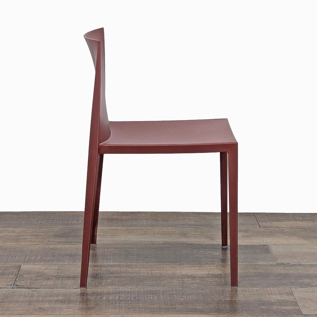 Side view of a sleek red plastic chair by Andreu World, showcasing its stackable design.