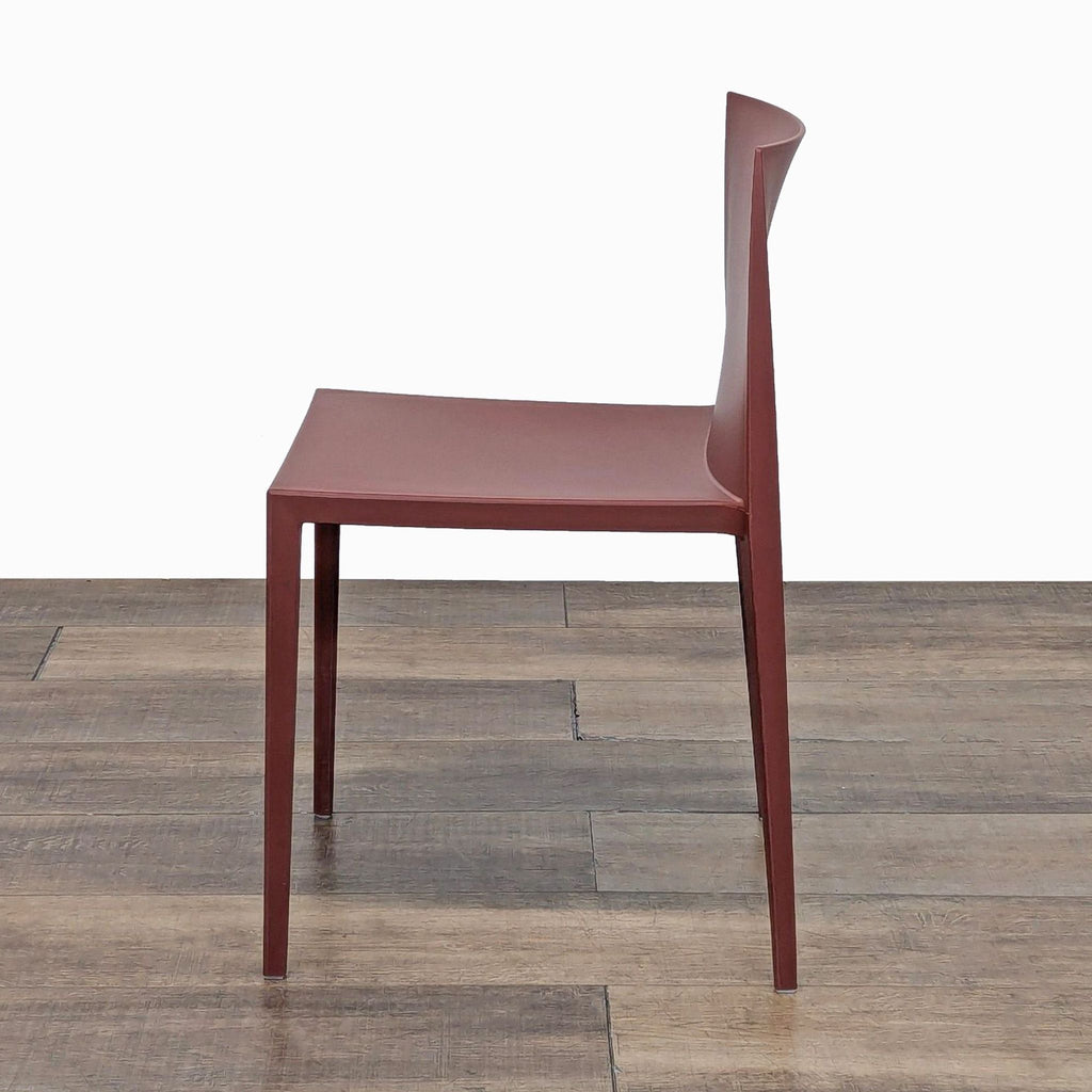 Another side view of the red stackable plastic chair by Andreu World on wood floor.