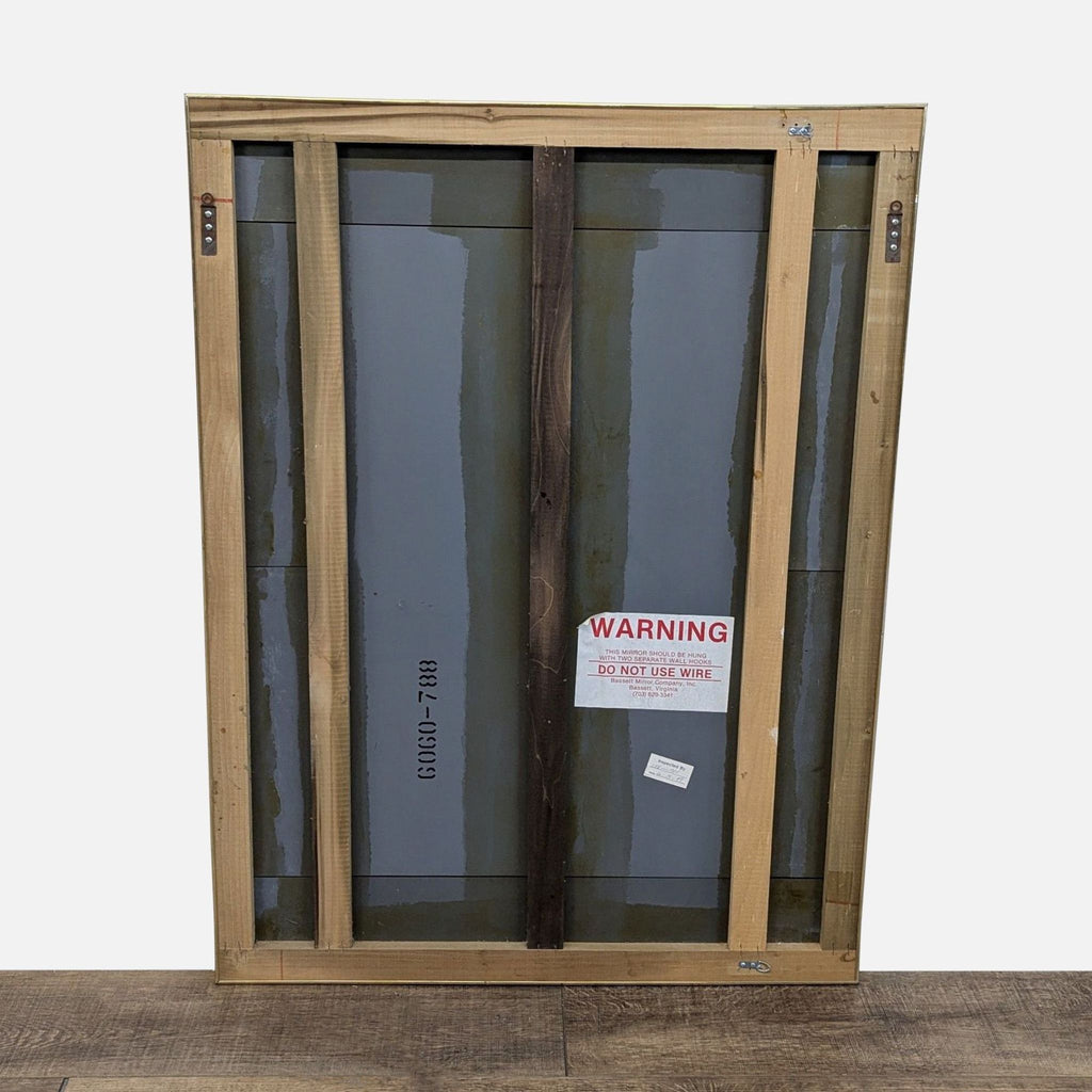 Back view of the Bassett Mirror showing wooden supports and a warning label.