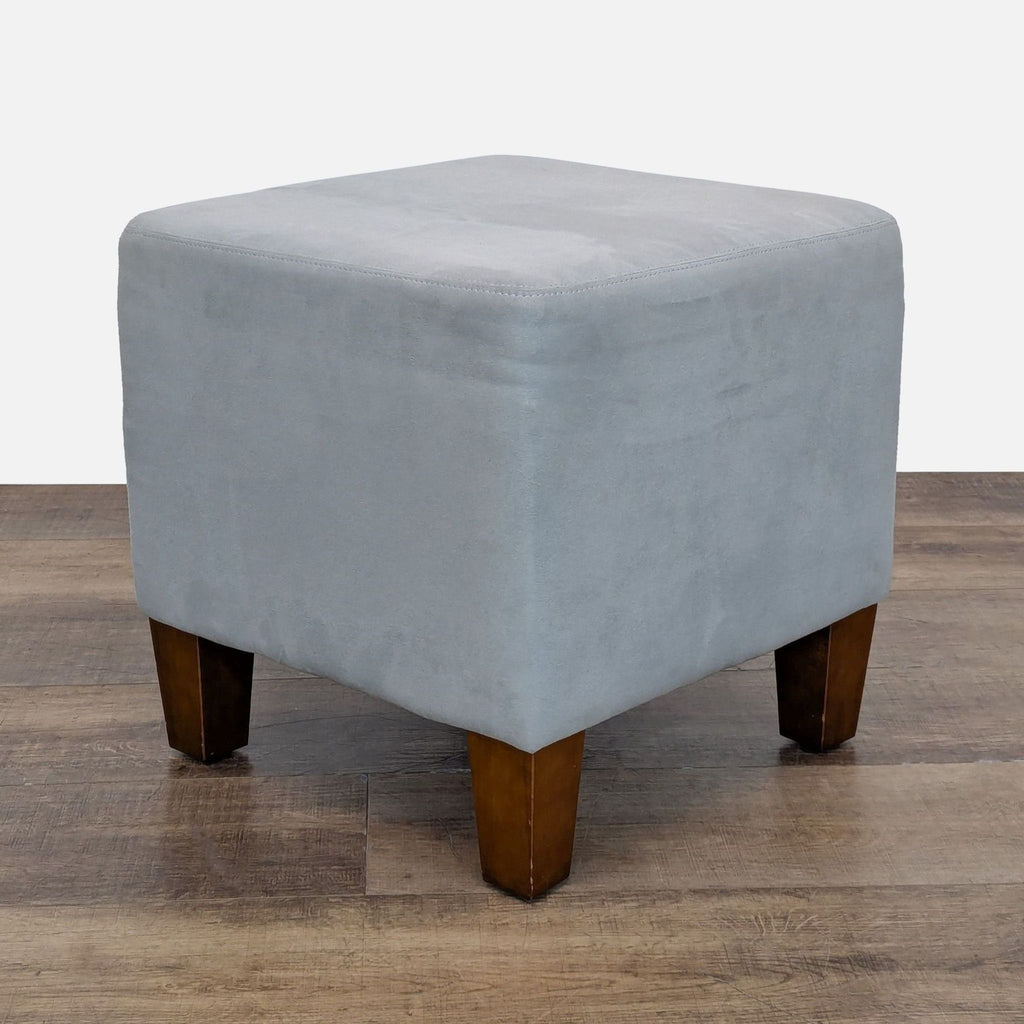 Light blue suede ottoman with wooden legs on a wooden floor.