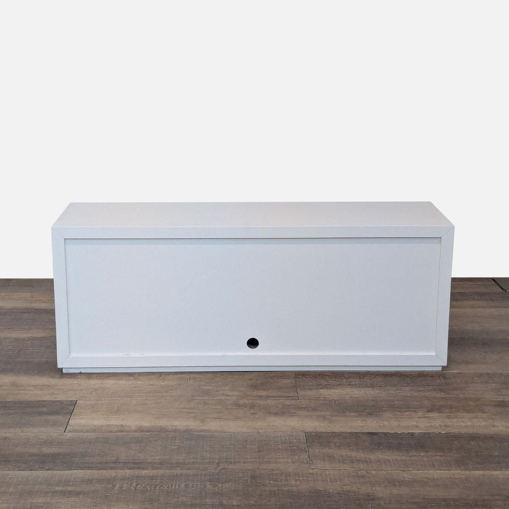 Back view of white rectangular cabinet on wooden floor with a small round hole near the bottom.  