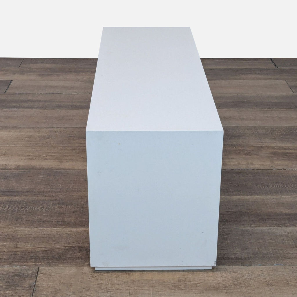 Side view of a plain white rectangular cabinet showing its depth and minimalist design on wooden floor.