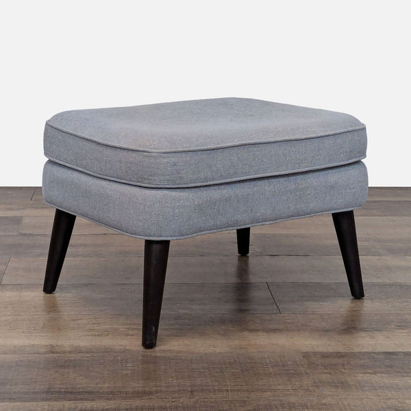 Gray upholstered ottoman with removable legs, on a wooden floor.