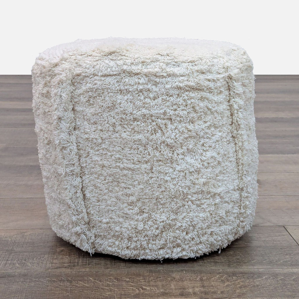 Round pouf in faux sheepskin, 100% cotton, on wooden floor.