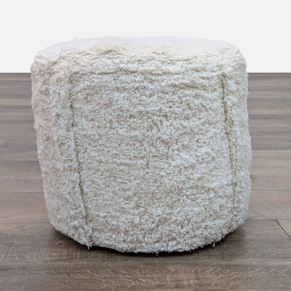 Round pouf in faux sheepskin, 100% cotton, on wooden floor.