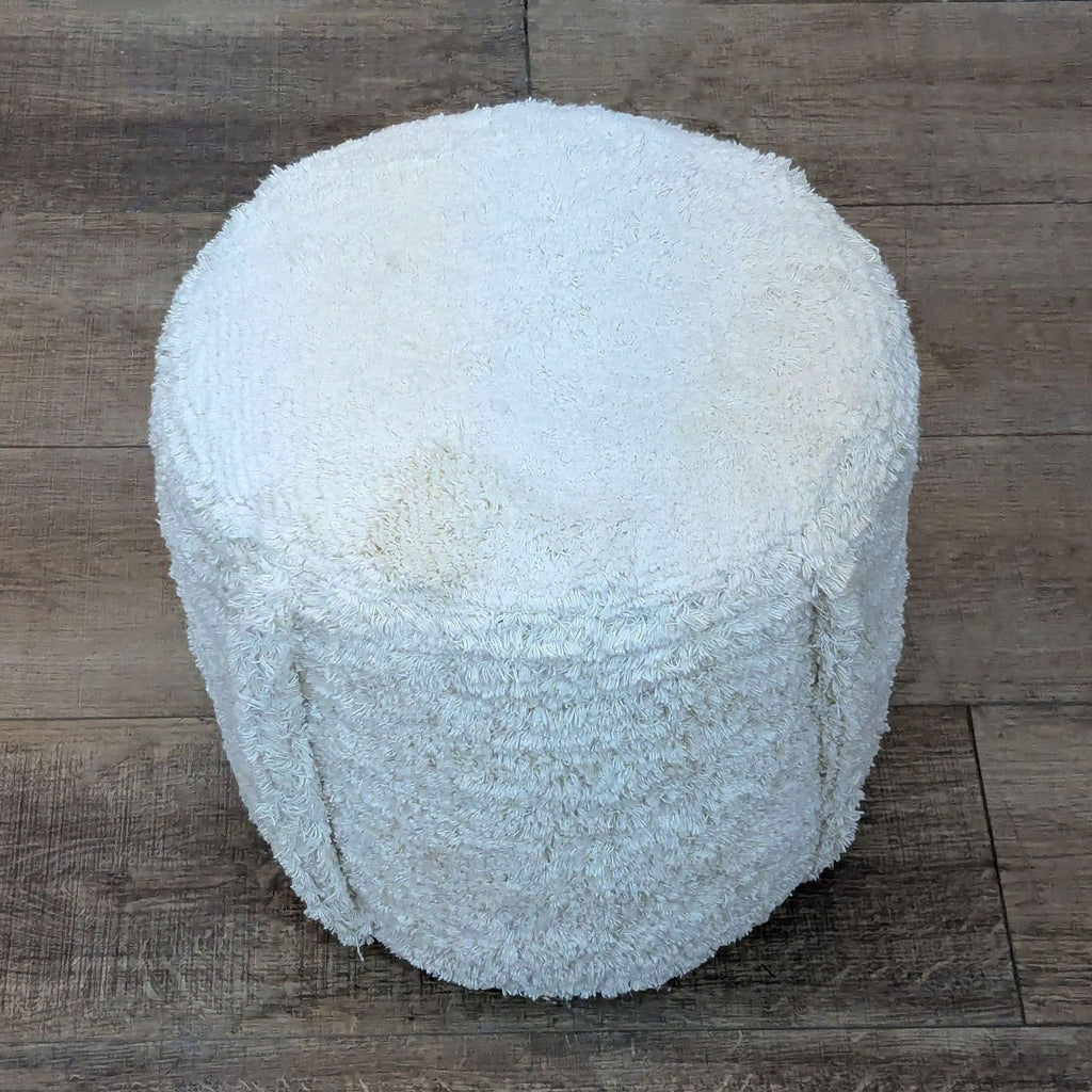 Cotton faux sheepskin pouf on a textured wooden surface.