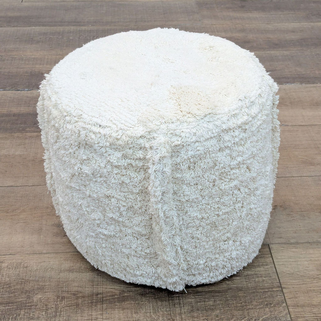 Side view of a faux sheepskin pouf, cylinder-shaped.