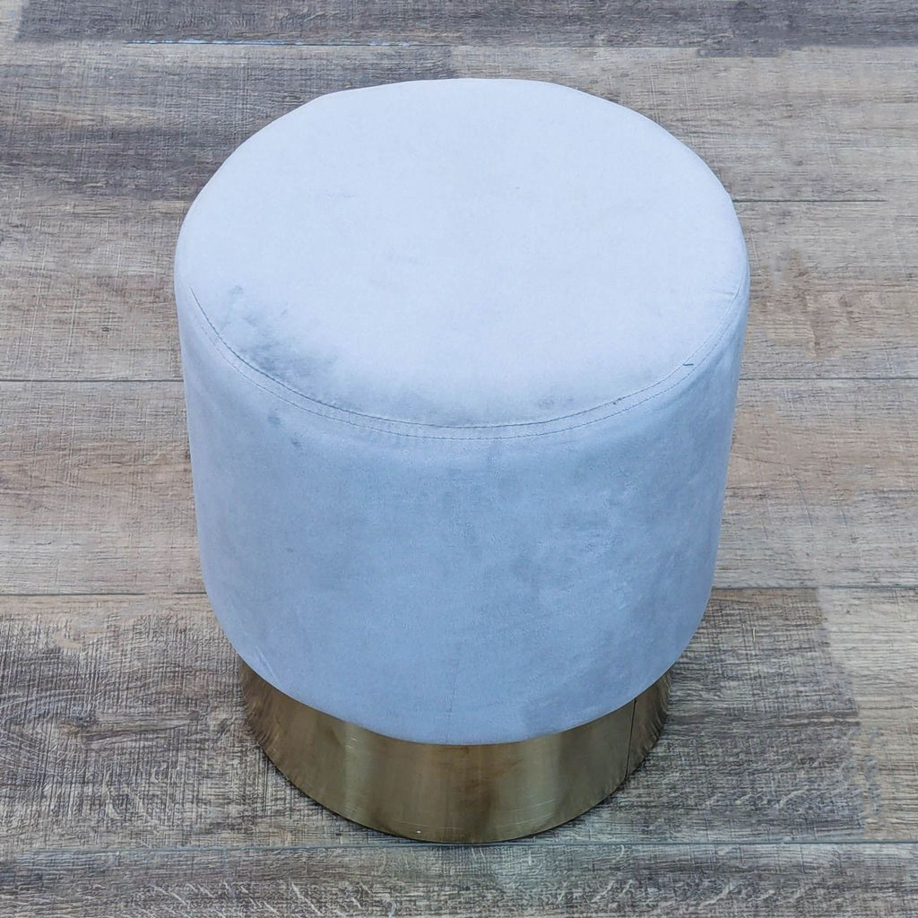 Top view of a round gray stool with velvet upholstery and a brass base, placed on a wooden floor.