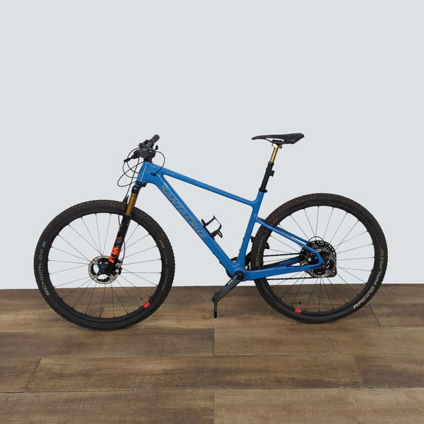 Blue carbon fiber hardtail mountain bike on wooden floor.