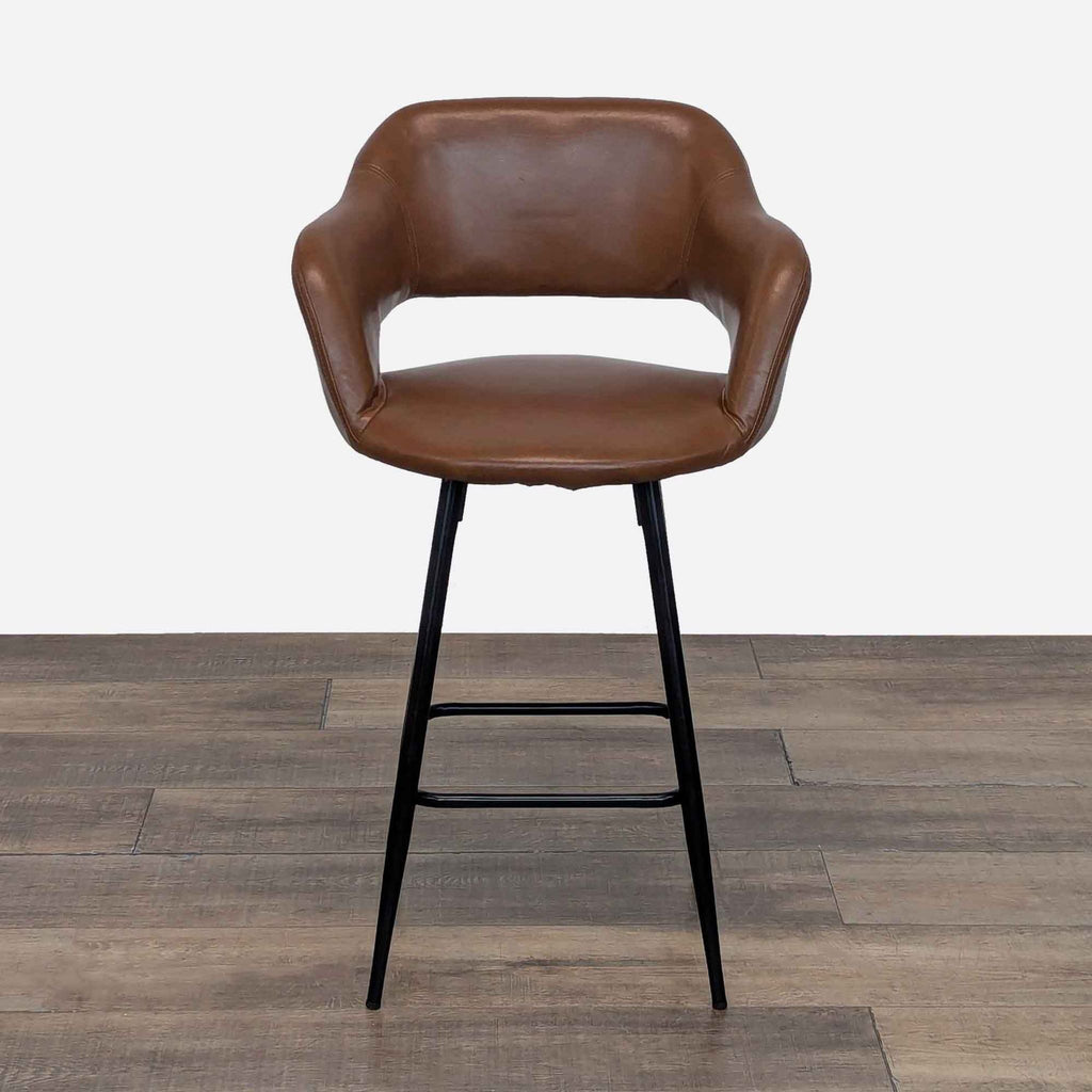 Brown leather stool with a curved back and black legs on wooden floor.