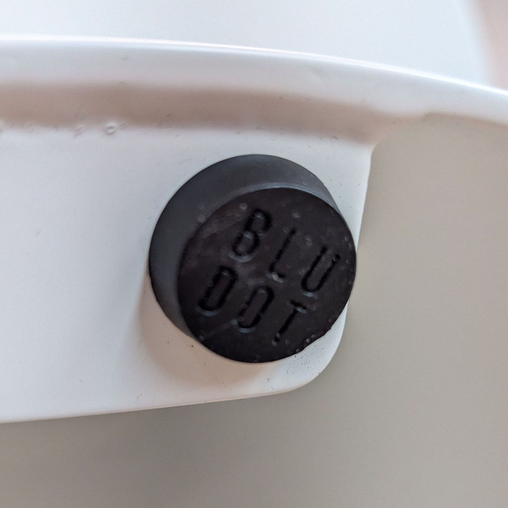 3. Detail of a black plastic foot on the underside of the Reperch metal table, imprinted with “BLU DOT”.