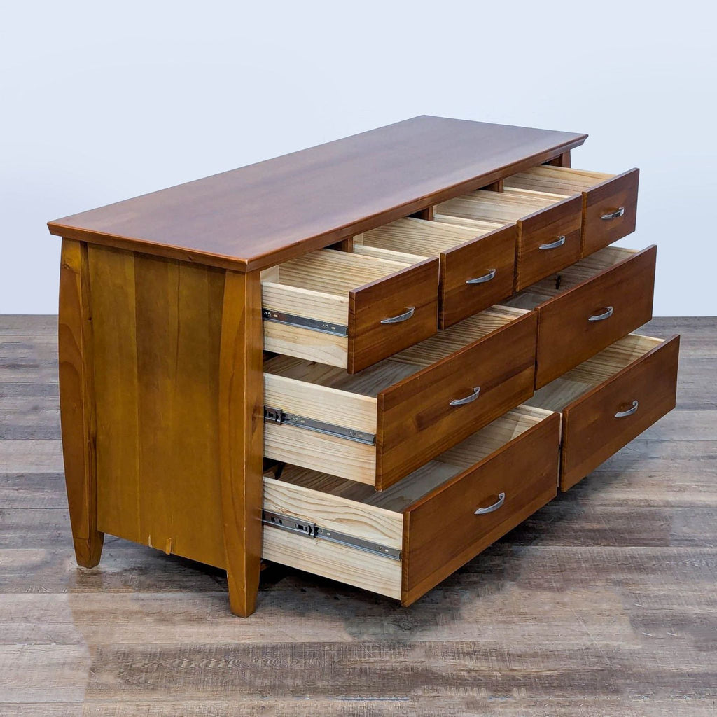 Side view of a wood dresser with open drawers and brushed nickel handles.