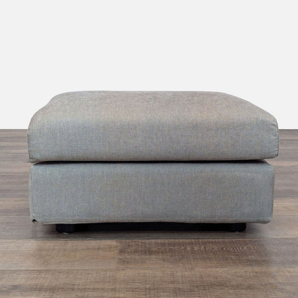 Gray ottoman with a simple, modern design on wooden floor.  