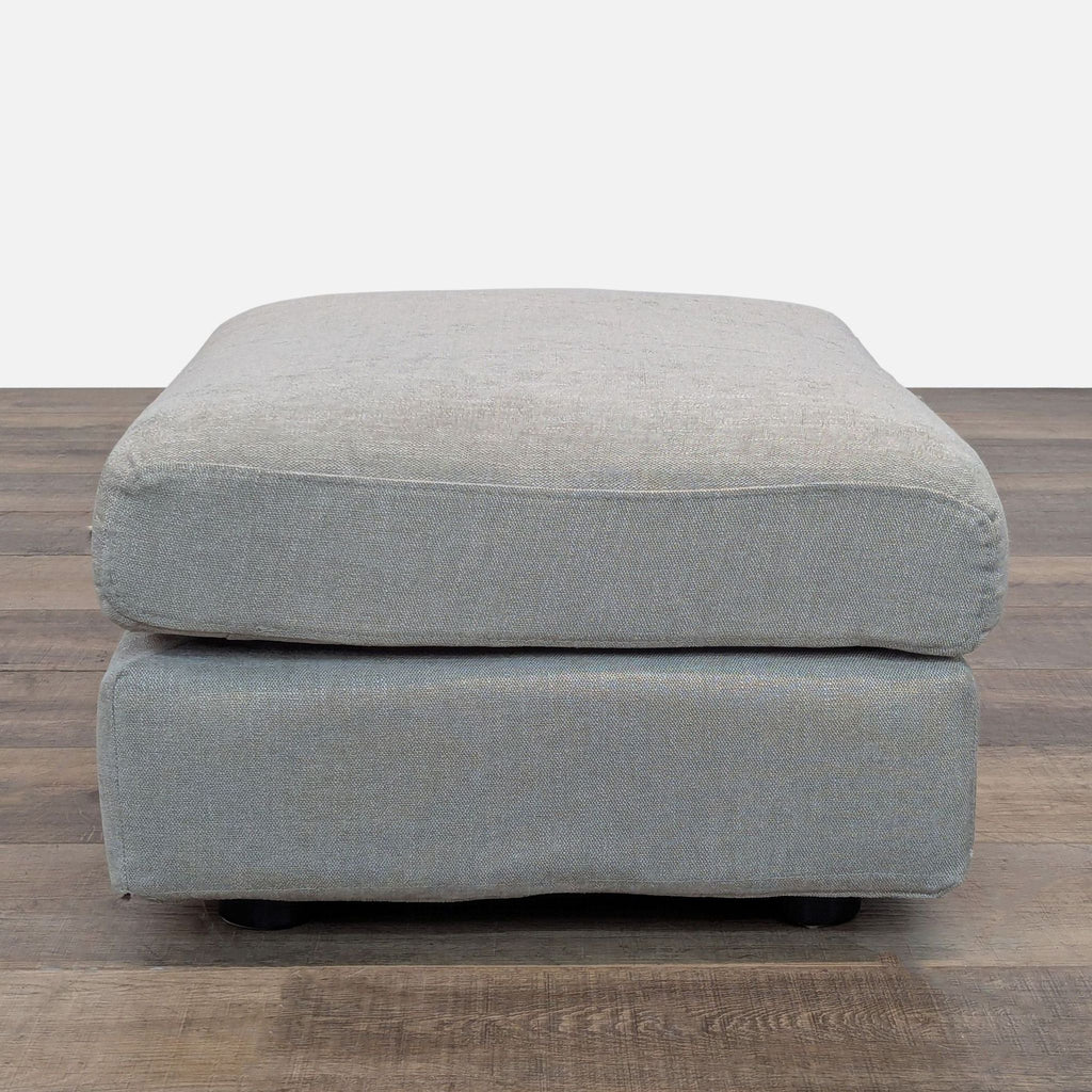 Square gray ottoman, ideal for modern interiors, on wood flooring.  