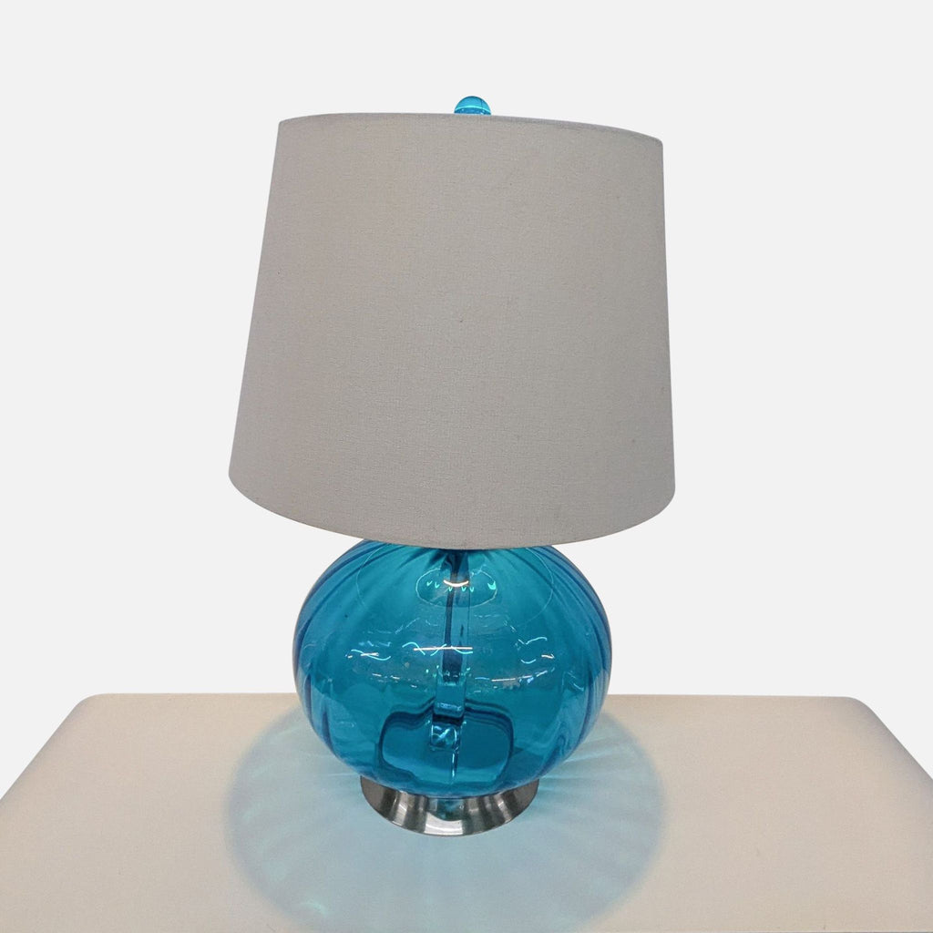 1. Pier 1 lamp with a round blue glass globe base, fabric shade, and matching blue finial on a table.  