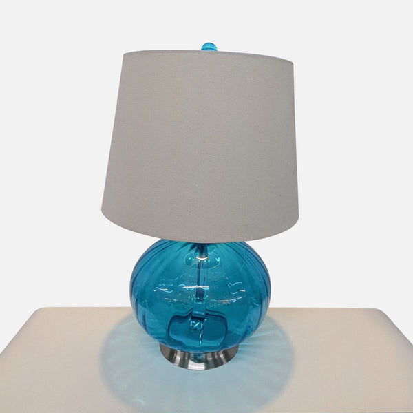 1. Pier 1 lamp with a round blue glass globe base, fabric shade, and matching blue finial on a table.  