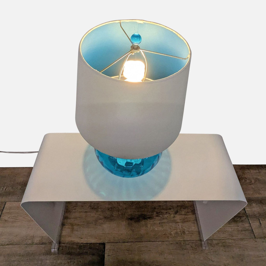 2. Overhead view of Pier 1 blue glass lamp lit, showing round base, white fabric shade, and blue finial.  