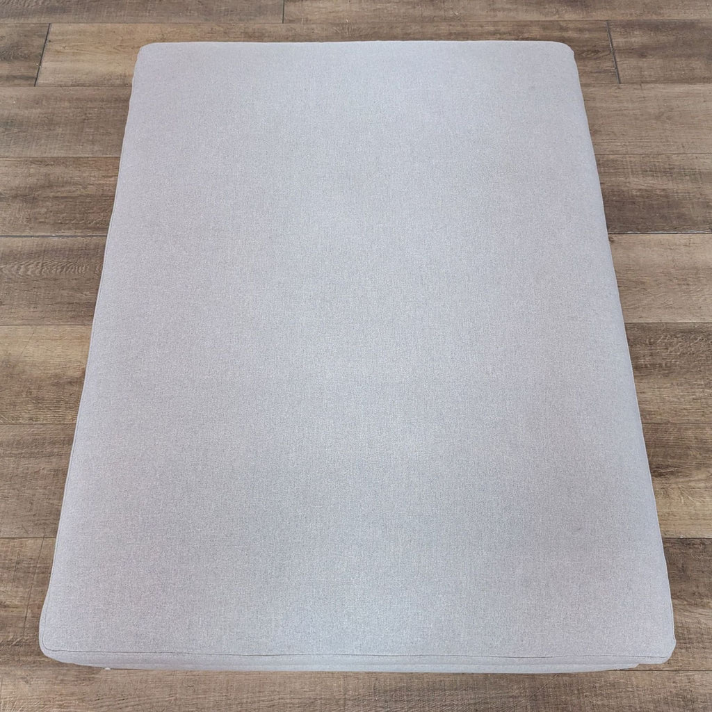 Top view of Rejuvenation Felton ottoman in soft cashmere flannel on wooden floor.