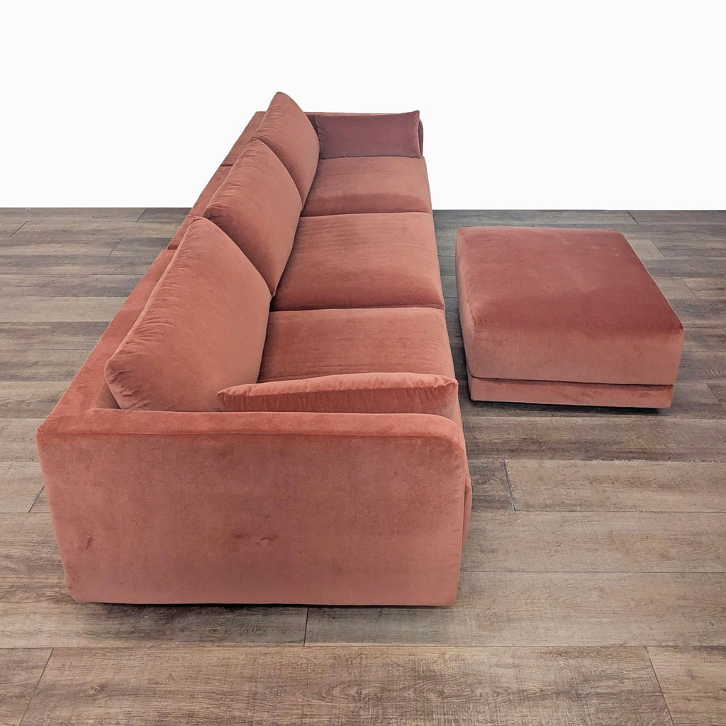 2. Side angle of the plush BenchMade Modern Eva 3-seat velvet sofa and ottoman on wood flooring.