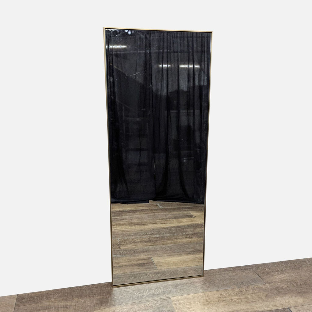 Brushed brass framed mirror with dark curtain backdrop.
