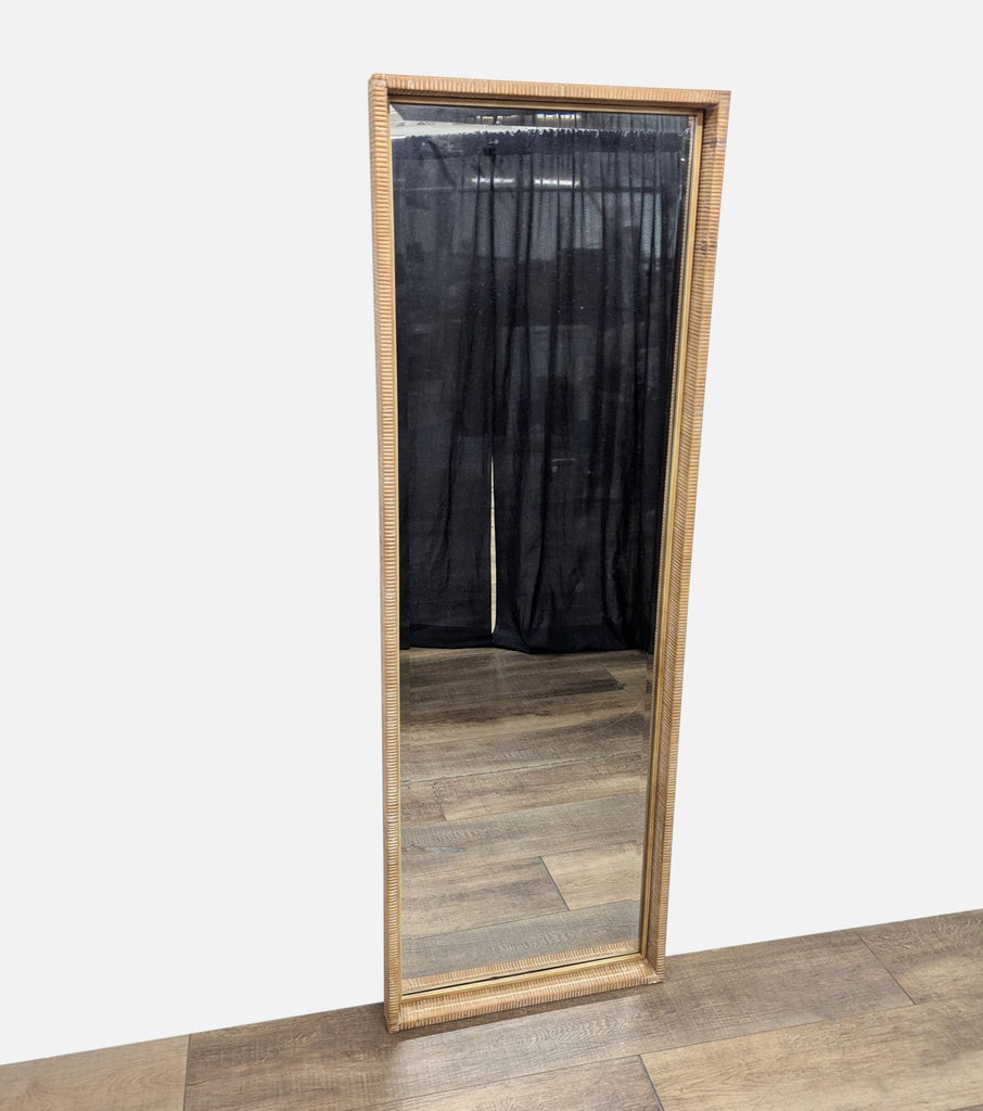 Tall rectangular mirror with a wooden frame, reflecting a room with black curtains.