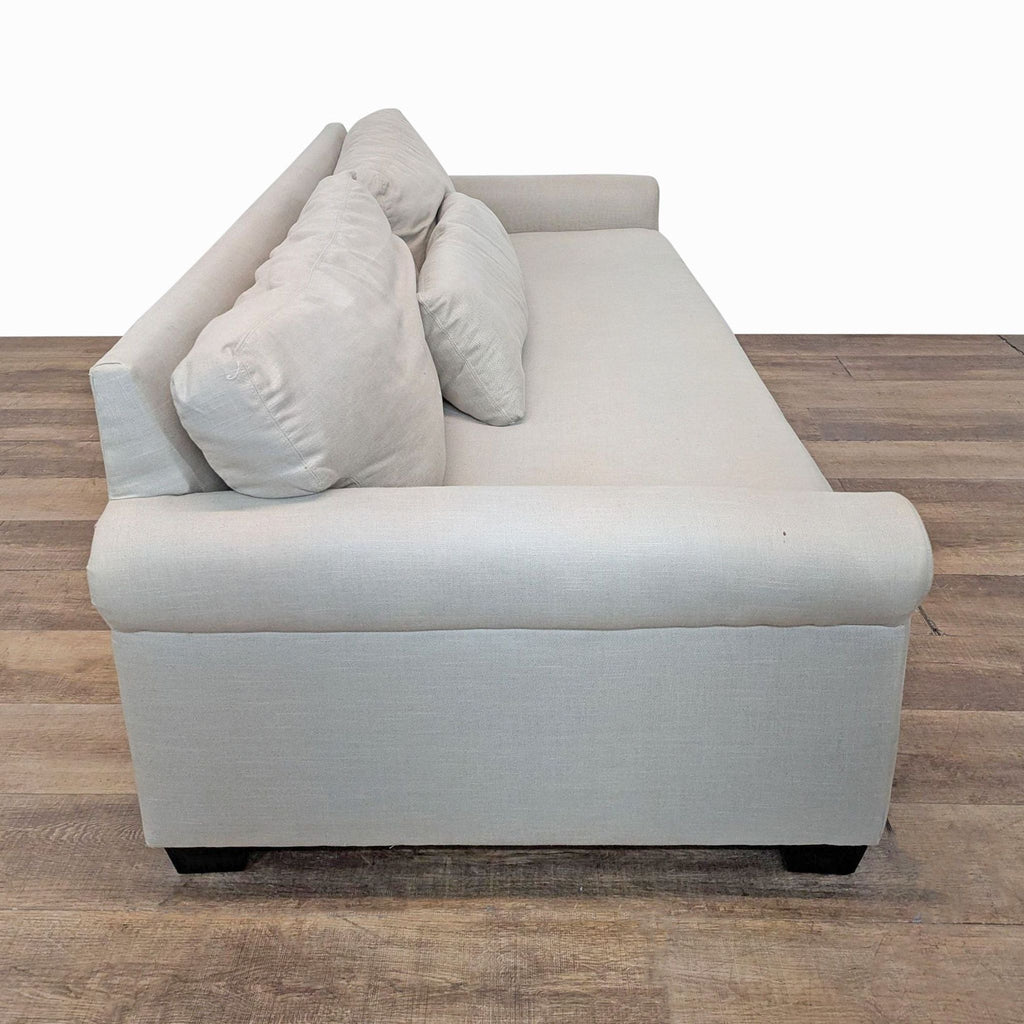 2. Side view of a light beige York 3-seat sofa by Pottery Barn with rolled arms and square tapered legs.  
