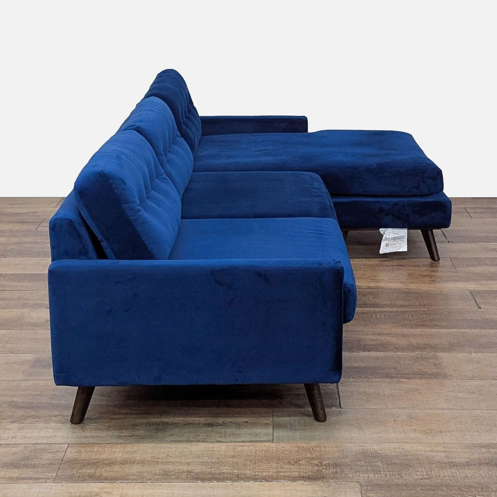 2. Side profile of a Royal Cobalt velvet Joybird sectional with tufted cushions and wood legs.