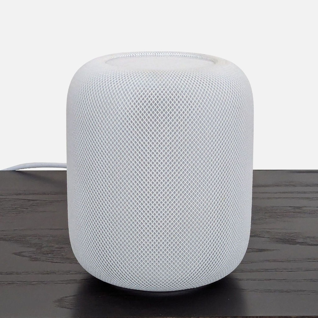 White Apple HomePod smart speaker with mesh exterior shown on a dark wooden table, front view.  