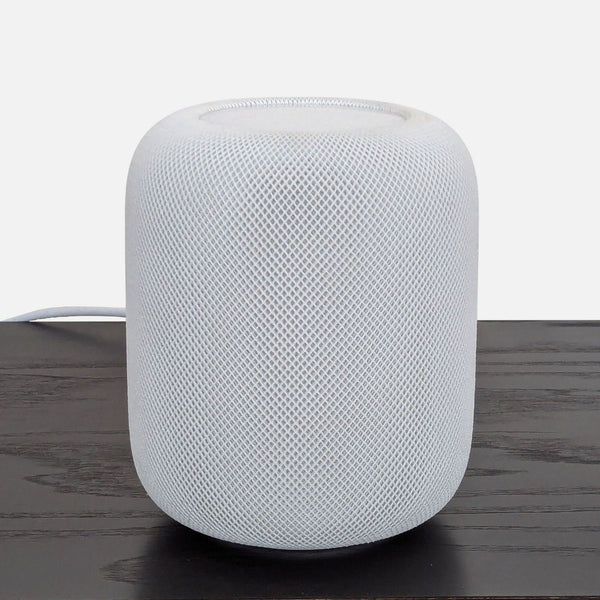 White Apple HomePod smart speaker with mesh exterior shown on a dark wooden table, front view.  