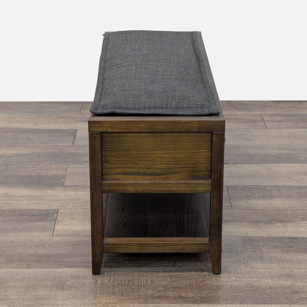 3. Side view of a Room & Board wooden ottoman with a cushioned seat and under-shelf for extra storage.