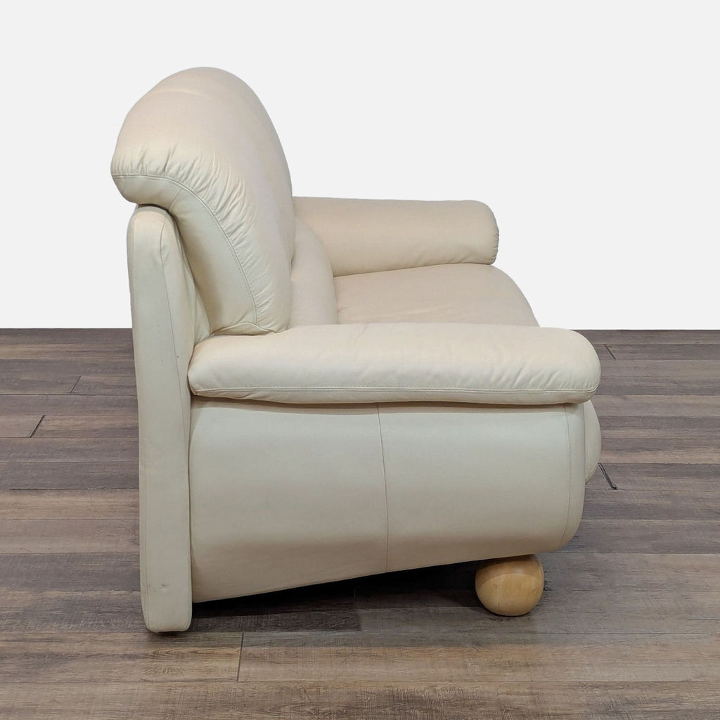 Side view of Reperch 3-seat sofa showing soft cream leather, curved arms, and distinctive wooden ball feet.